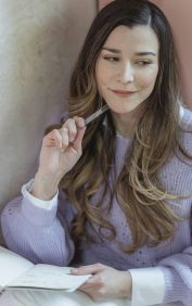 Woman with long hair daydreaming while writing notes indoors. Warm and inviting atmosphere.